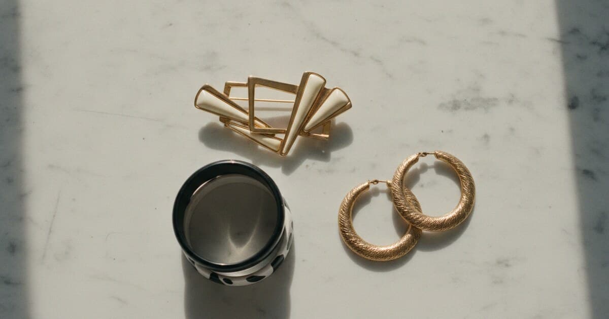 Vintage 1960s Mod jewelry including bold geometric enamel bangles, large hoop earrings, and a statement brooch arranged on a white marble surface