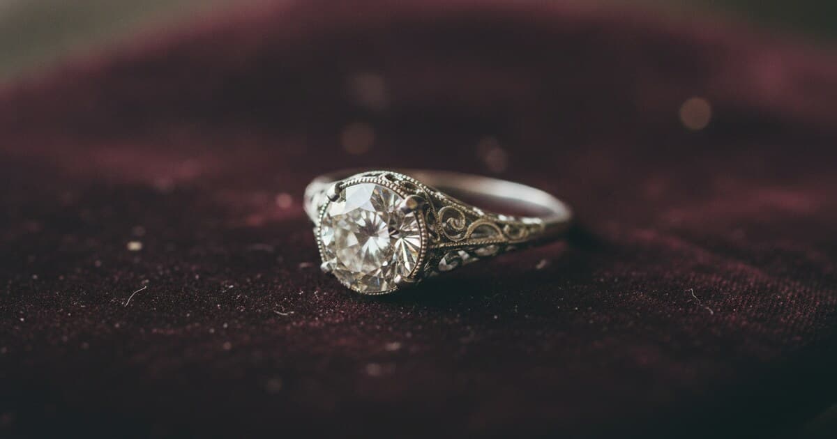 Close-up of an antique diamond ring with an old European cut stone in a platinum filigree setting, photographed on aged velvet