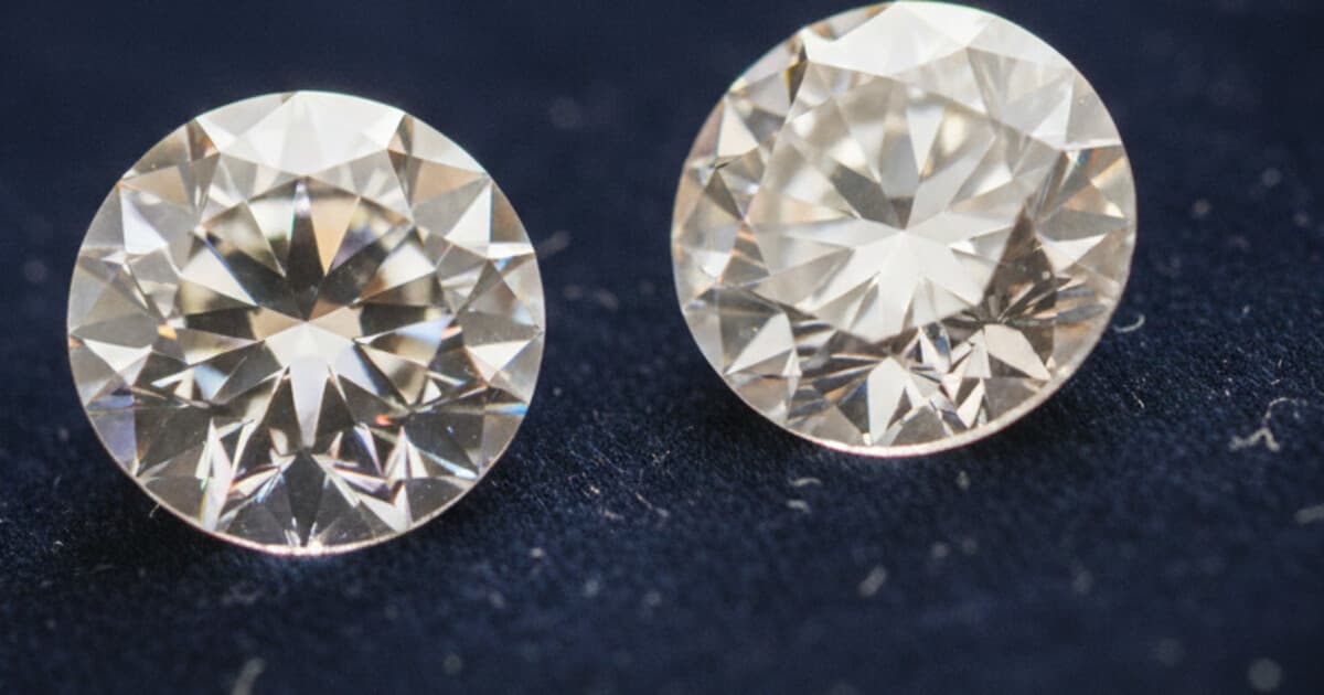 Round brilliant diamond and cubic zirconia side by side on dark navy velvet