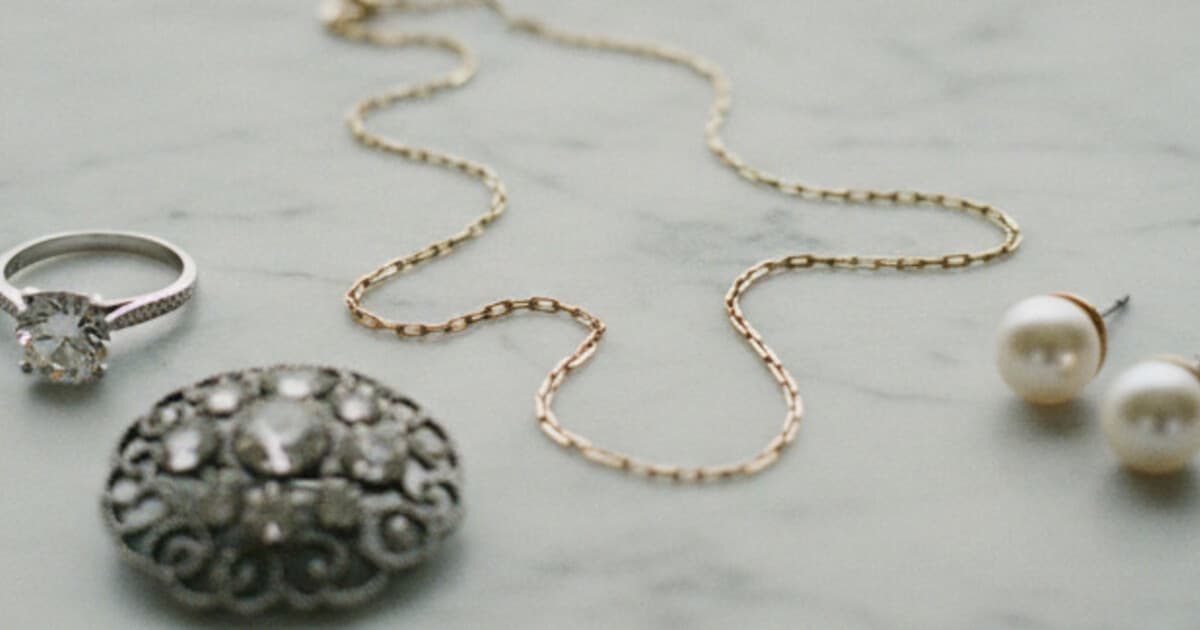 Assorted jewelry pieces for eBay sale including gold chain, diamond ring, vintage brooch, and pearl earrings on white marble