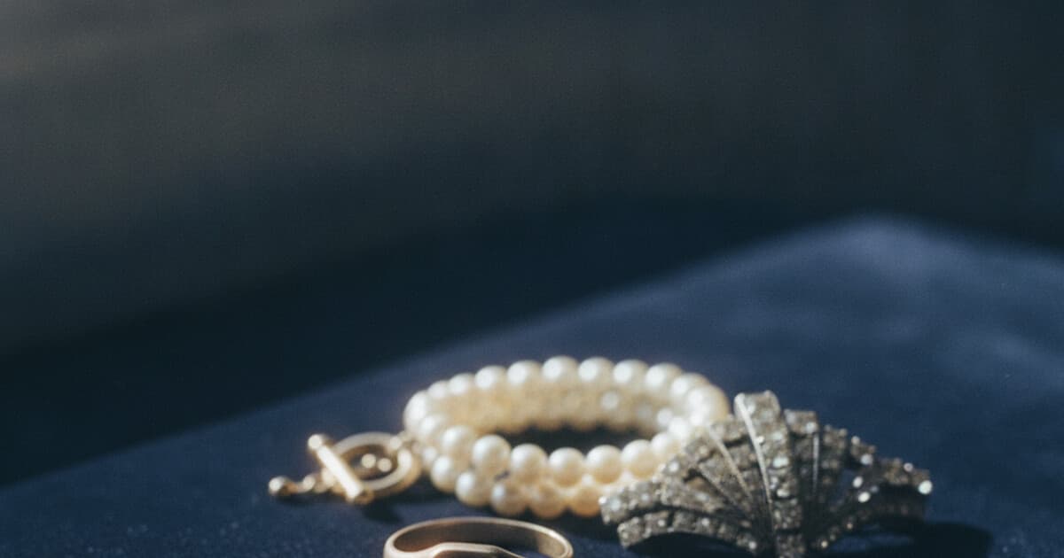 Close-up of antique gold jewelry pieces and a pearl necklace arranged on navy velvet for identification
