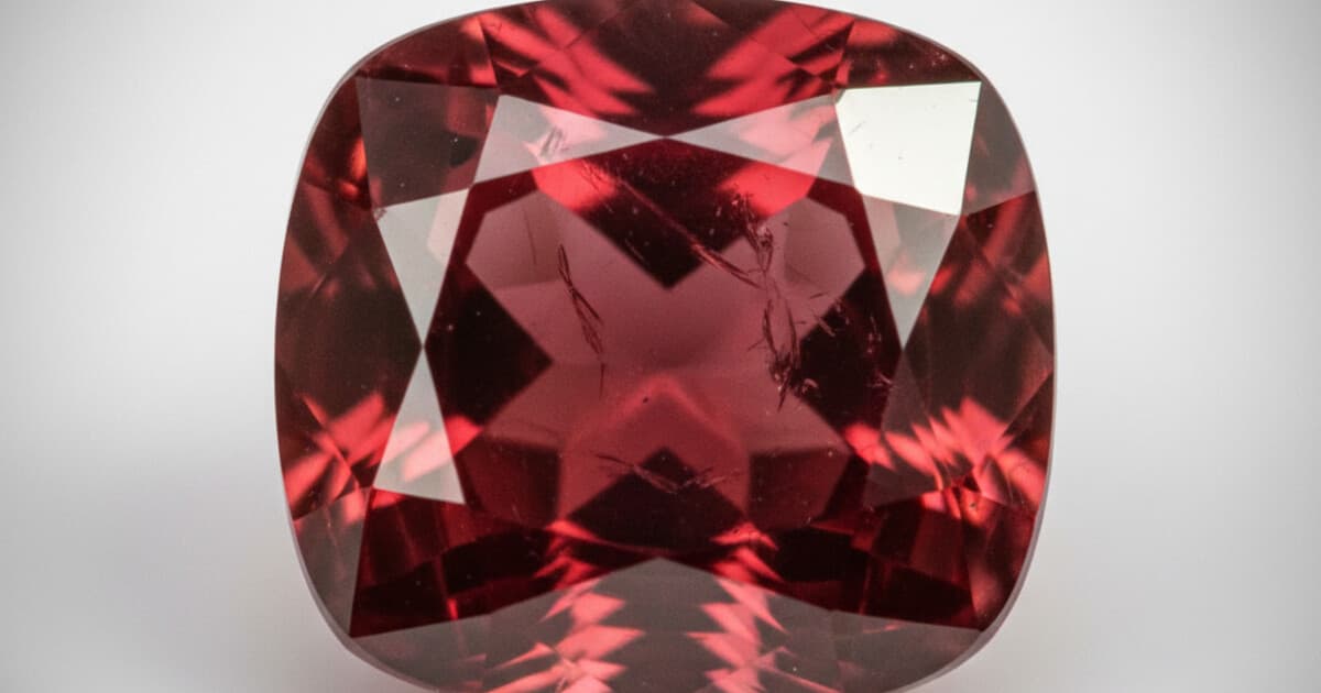 Deep red faceted garnet gemstone on a white background showing natural inclusions and rich color