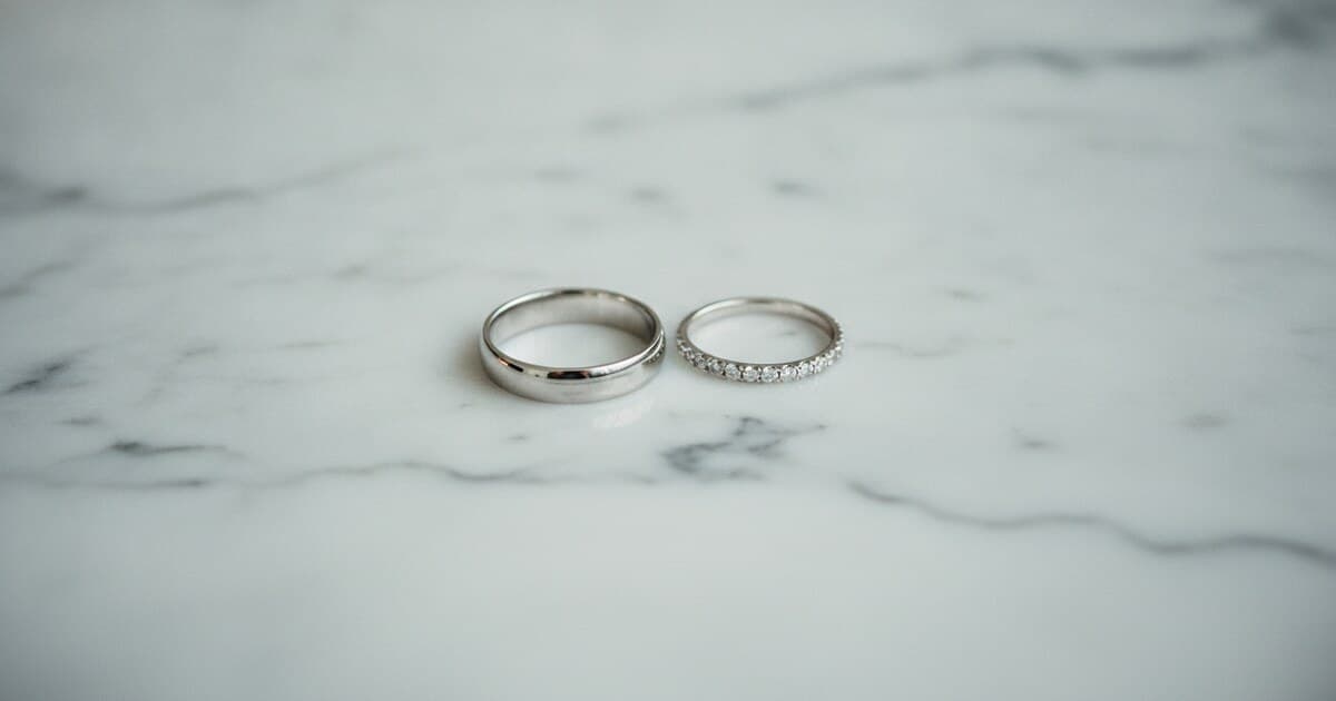 Sterling silver band and white gold diamond ring side by side on white marble surface