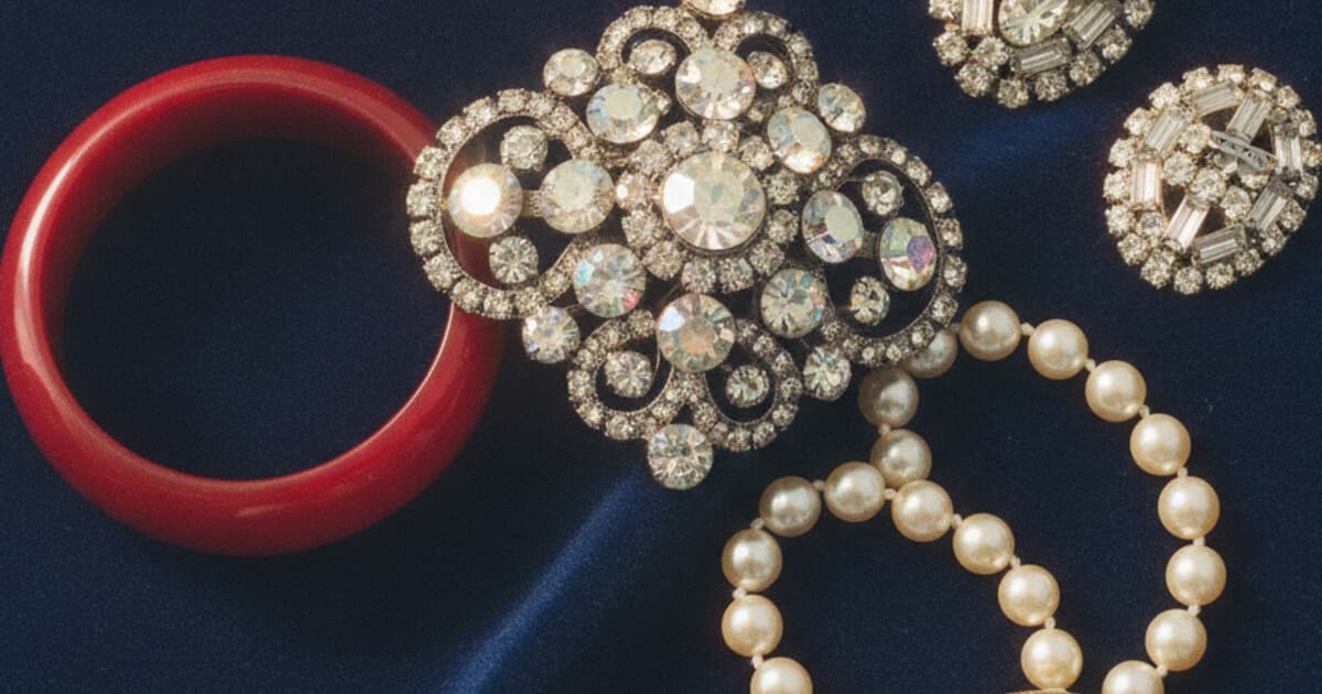 Overhead view of vintage rhinestone brooch, Bakelite bangle, and signed costume jewelry pieces arranged on dark navy velvet