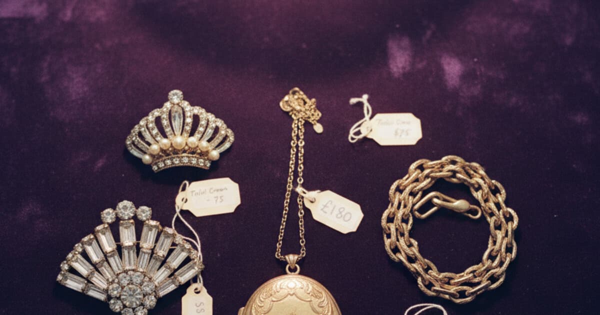 Collection of vintage jewelry pieces on velvet: Victorian locket, Art Deco brooch, mid-century Trifari pin, and gold bracelet at an antique market
